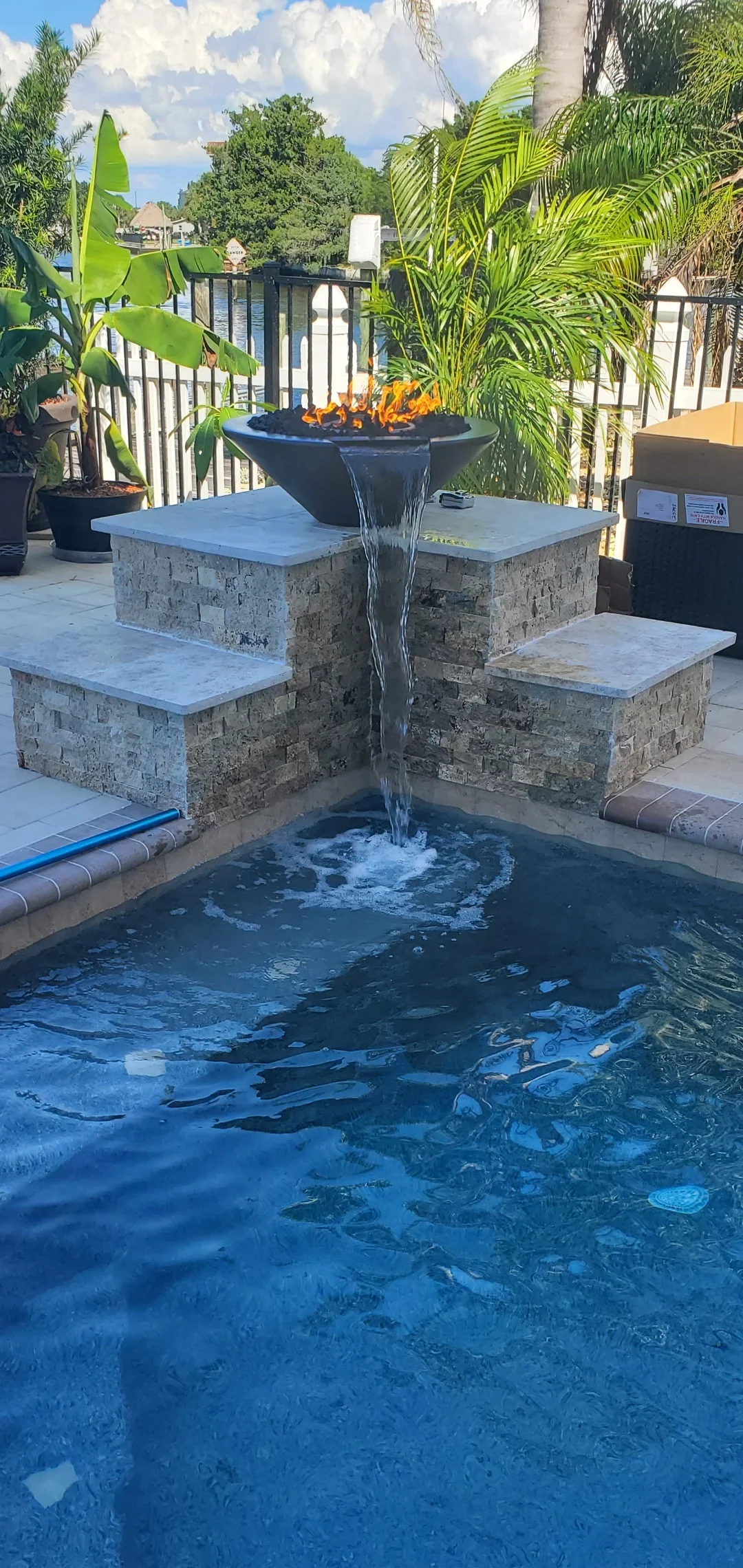 In-ground pool with fire bowl, stone seating bench, blue coping, and tropical plants