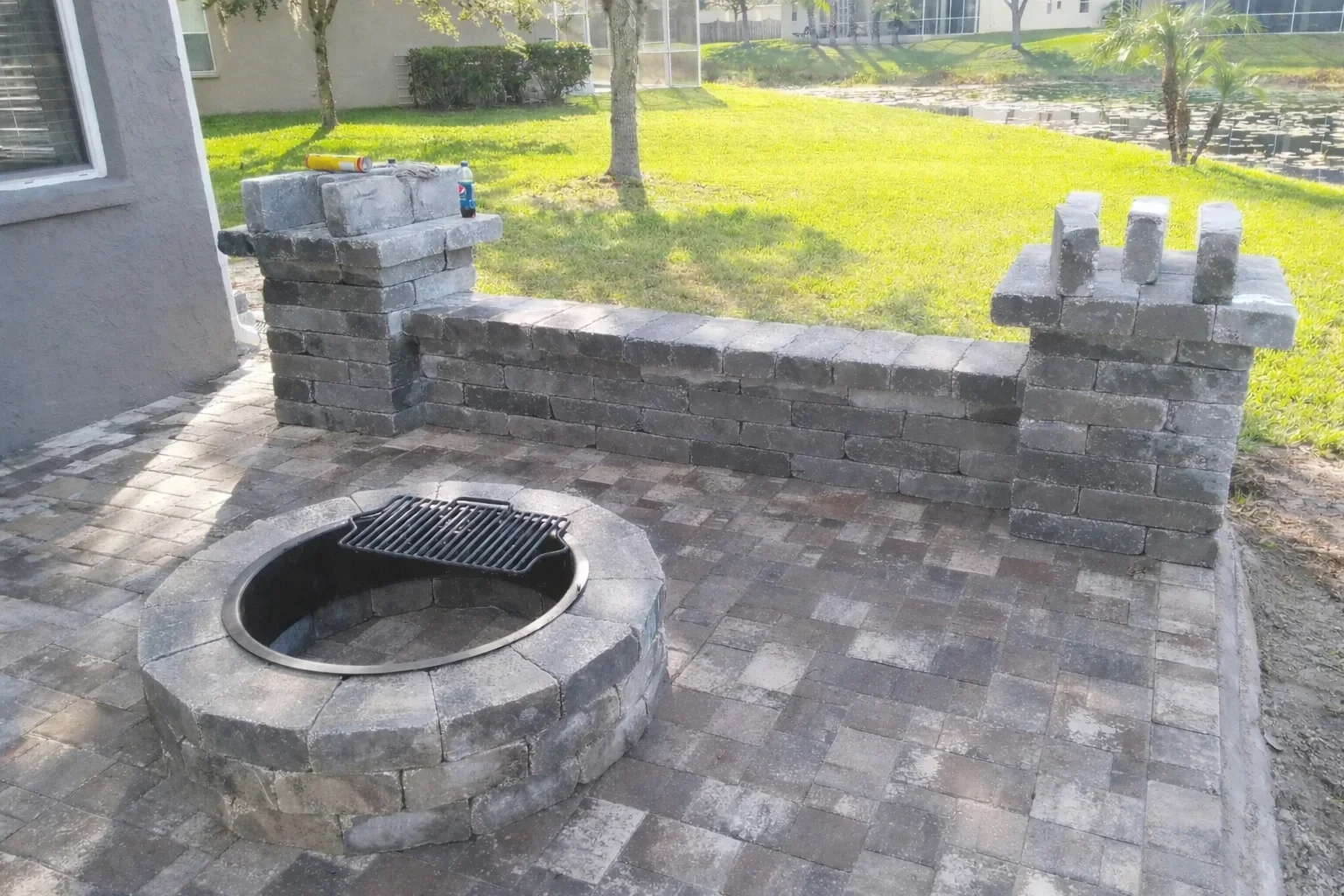 Gray concrete block retaining wall with bench seating and circular fire pit on paver patio